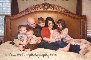 family of 6 on bed looking at newborn baby girl
