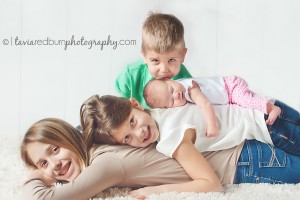siblings with their newborn baby sister, laying on each other with brother kissing
