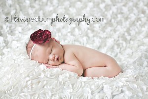 baby girl newborn posed on white rose ruffle blanket with red headband