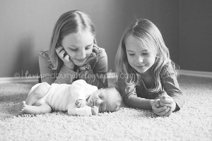 newborn baby brother laying down in front of his big sisters