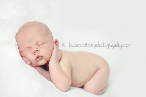 newborn baby boy posed on white blanket with hands on his cheeks