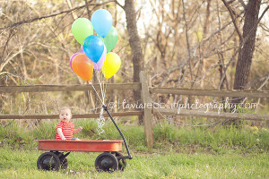 1 year old in a red wagon with balloons
