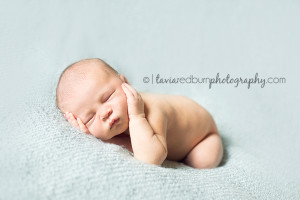 newborn baby boy posed on blue blanket, hands on face, sleeping