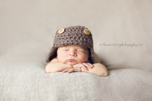 newborn baby boy with brown aviator hat, posed with head on hands