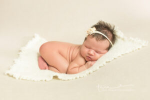 Newborn in Oklahoma City for her professional portrait session laying on a white blanket curled up and sleeping