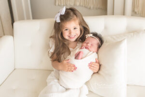 Big sister proudly holding her newborn sister in oklahoma city portrait session